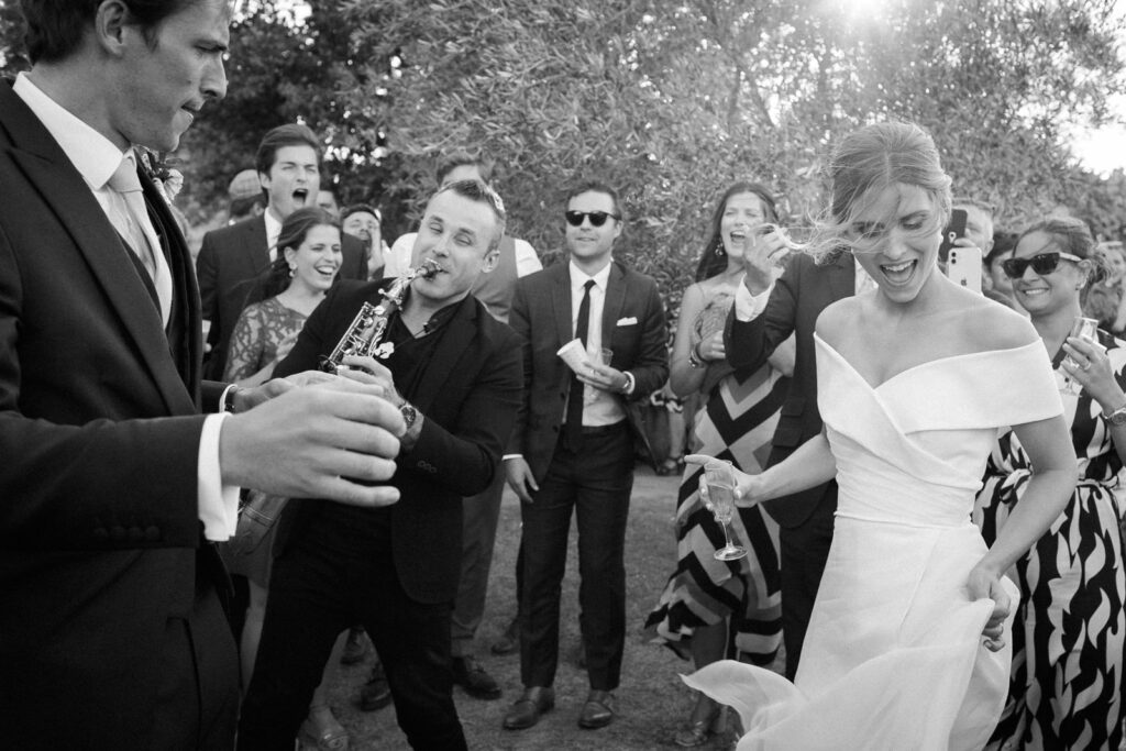 Bride laughing with guests and live saxophone during cocktail hour at a wedding reception in Provence, south of France